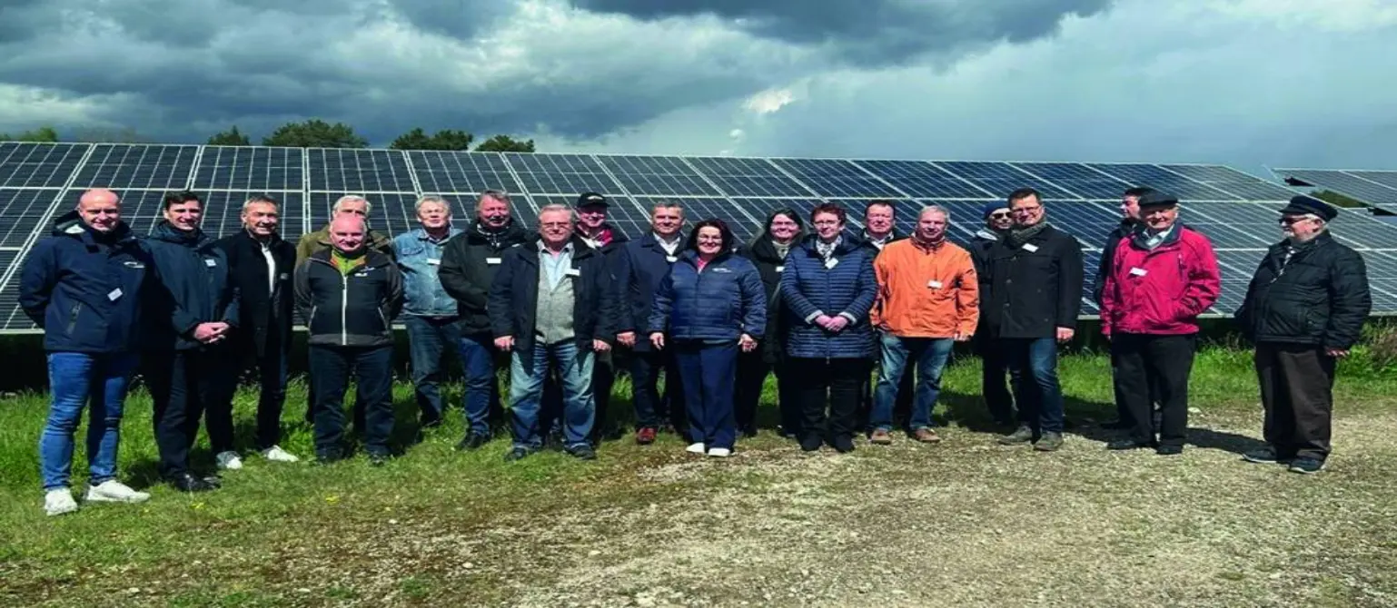 Eine Gruppe von 20 Personen in Freizeitkleidung steht vor den aufgereihten Paneelen des Solarparks Frauendorf in Brandenburg.