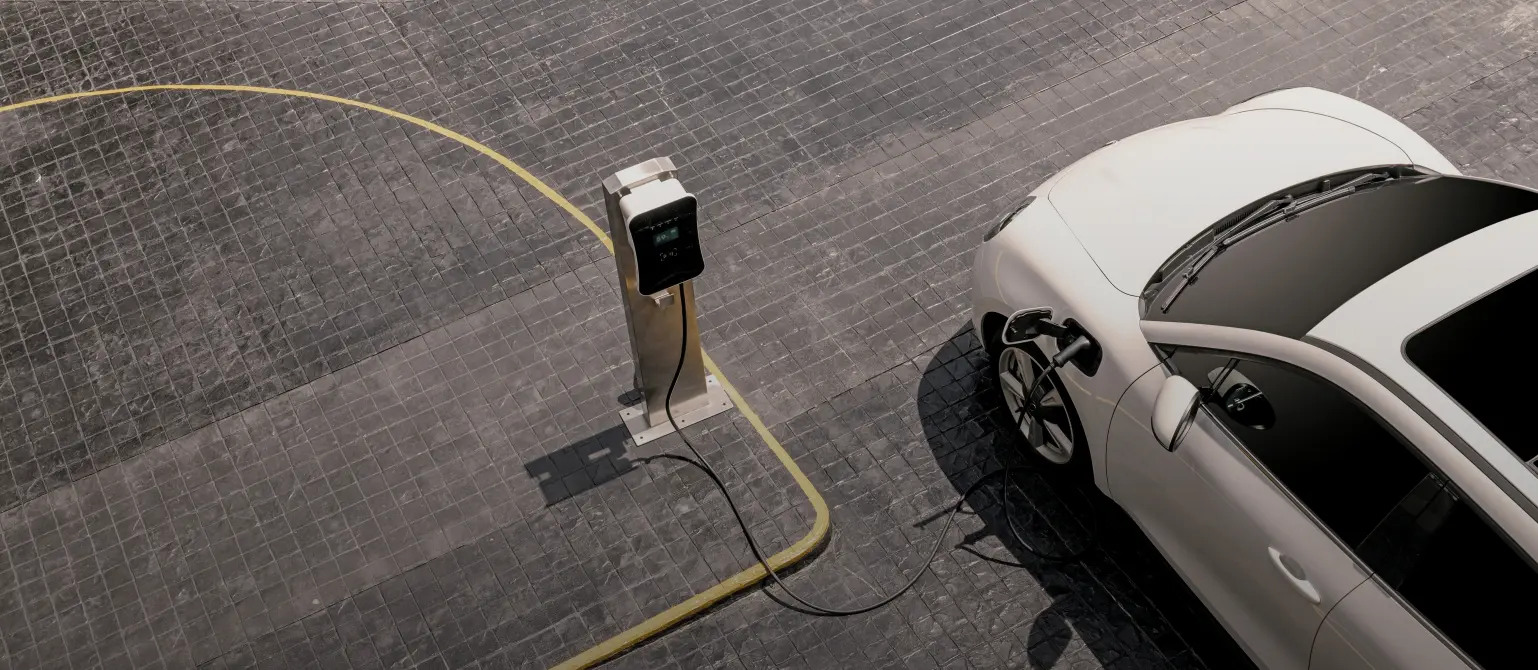 Ein weißes Auto von oben aufgenommen, steht auf einem Parkplatz. Oberhalb des linken Vorderrads wird das Fahrzeug an einer Ladesäule geladen.