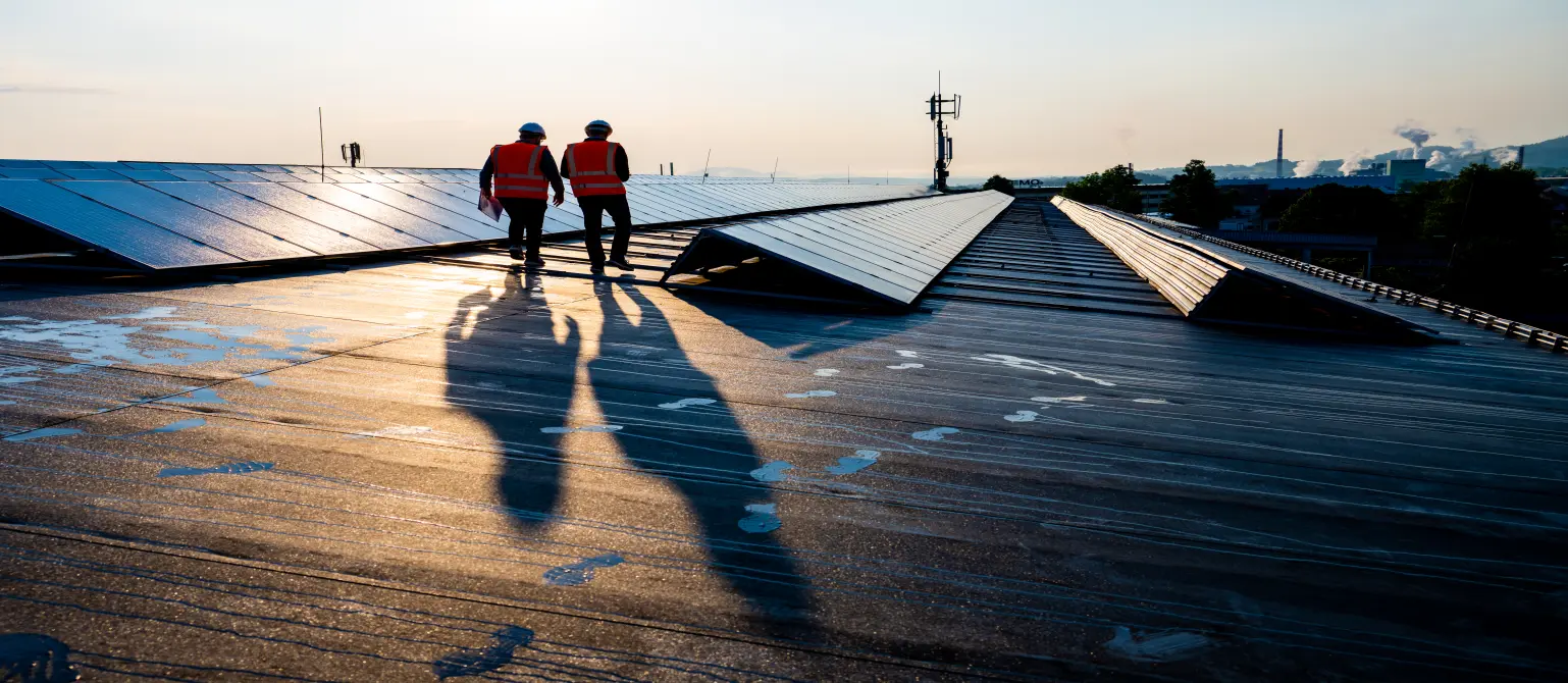 Abendstimmung: Zwei Installateure schlendern über ein sonniges Flachdach voller Solarmodule.