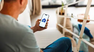 Blick über die Schulter einer Person auf das Handy auf dem das Logo von Energie Brandenburg ist.