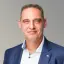 Porträtfoto Mirco Kostanski von Energie Brandenburg trägt ein blaues Sakko und ein helles Hemd.
