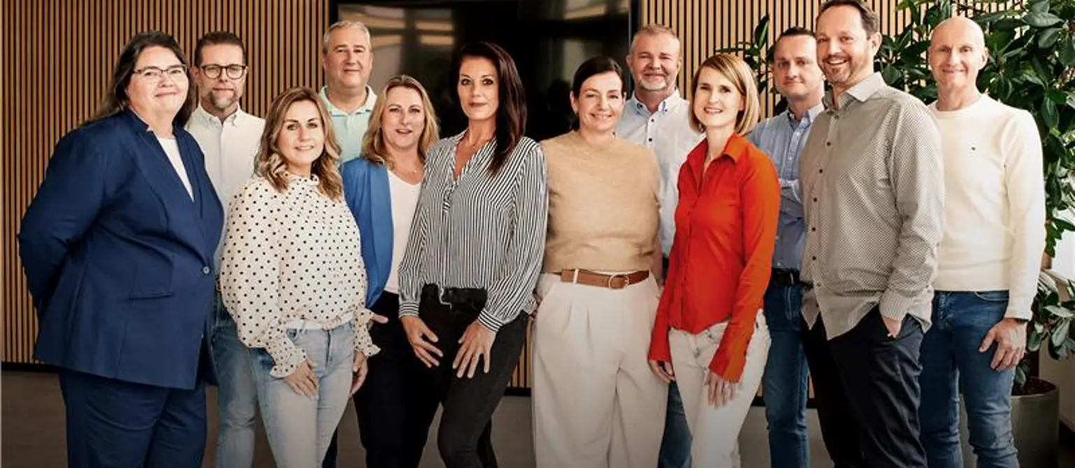 Gruppenfoto: Service-Team der Kundenbüros von Energie Brandenburg. Im Hintergrund ein Bildschirm, eine holzverkleidete Wand und eine Grünpflanze.