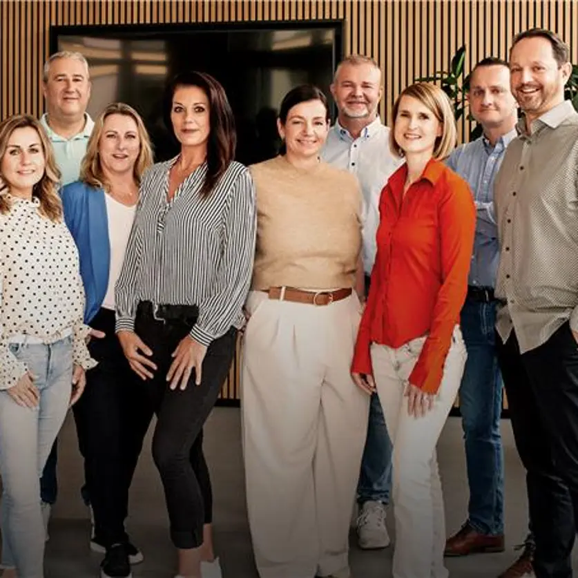 Gruppenfoto: Service-Team der Kundenbüros von Energie Brandenburg. Im Hintergrund ein Bildschirm, eine holzverkleidete Wand und eine Grünpflanze.
