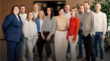 Gruppenfoto: Service-Team der Kundenbüros von Energie Brandenburg. Im Hintergrund ein Bildschirm, eine holzverkleidete Wand und eine Grünpflanze.