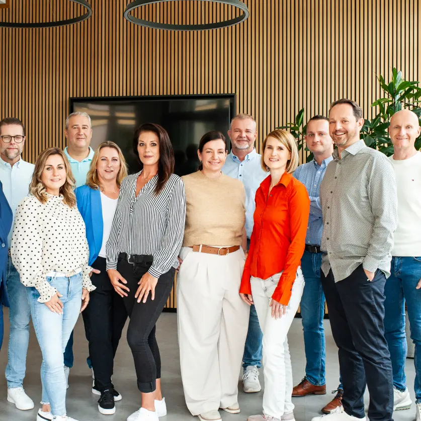 Gruppenfoto: Das Service-Team der Kundenbüros von Energie Brandenburg. Im Hintergrund ein Bildschirm, eine holzverkleidete Wand und eine Grünpflanze.