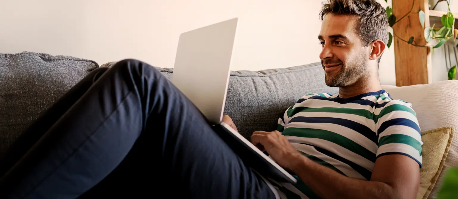 Ein Mann liegt auf der Couch mit seinem Laptop auf dem Schoß