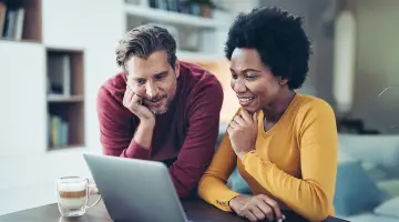 Ein Mann und eine Frau schauen neugierig und lächelnd in ihren Laptop