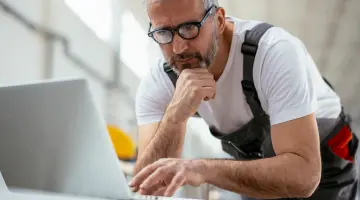 Newsletter Energie Brandenburg kompakt: Installateur mit Brille liest Newsletter am Laptop in der Werkstatt.