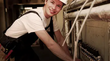 Ein Mann lächelt freundlich in die Kamera während er die leitungen im Keller prüft