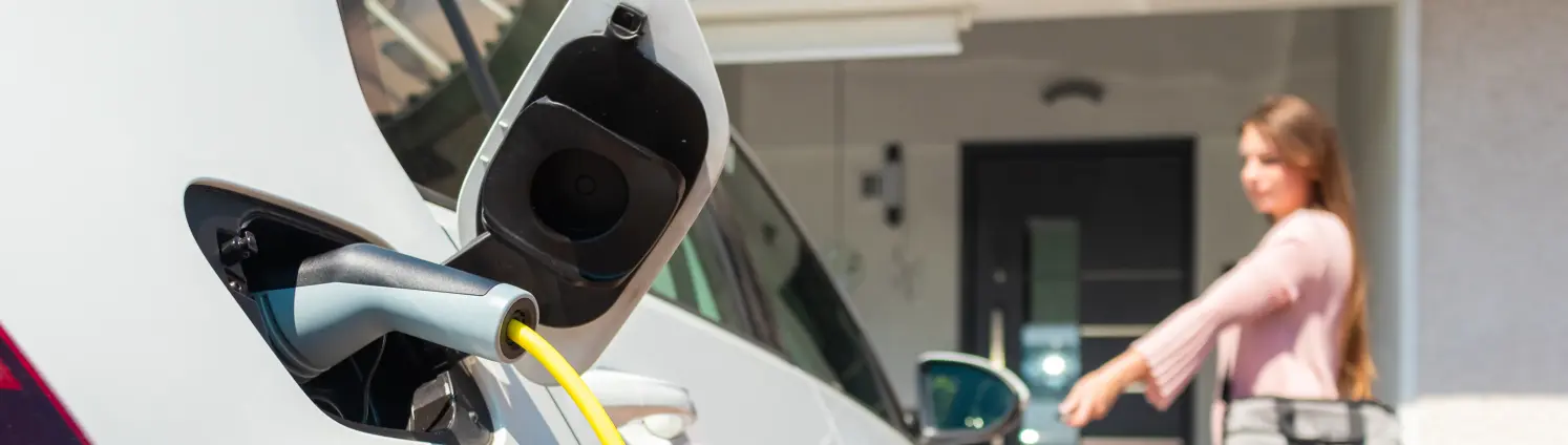Eine Frau schließt ein E-Auto ab, das gerade an einer Wallbox mit Strom aufgeladen wird.