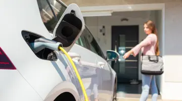Eine Frau schließt ein E-Auto ab, das gerade an einer Wallbox mit Strom aufgeladen wird.