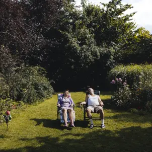 Ein älteres Ehepaar sitzt auf gepolsterten Gartenstühlen in der Sonne auf dem Rasen und macht ein Nickerchen.