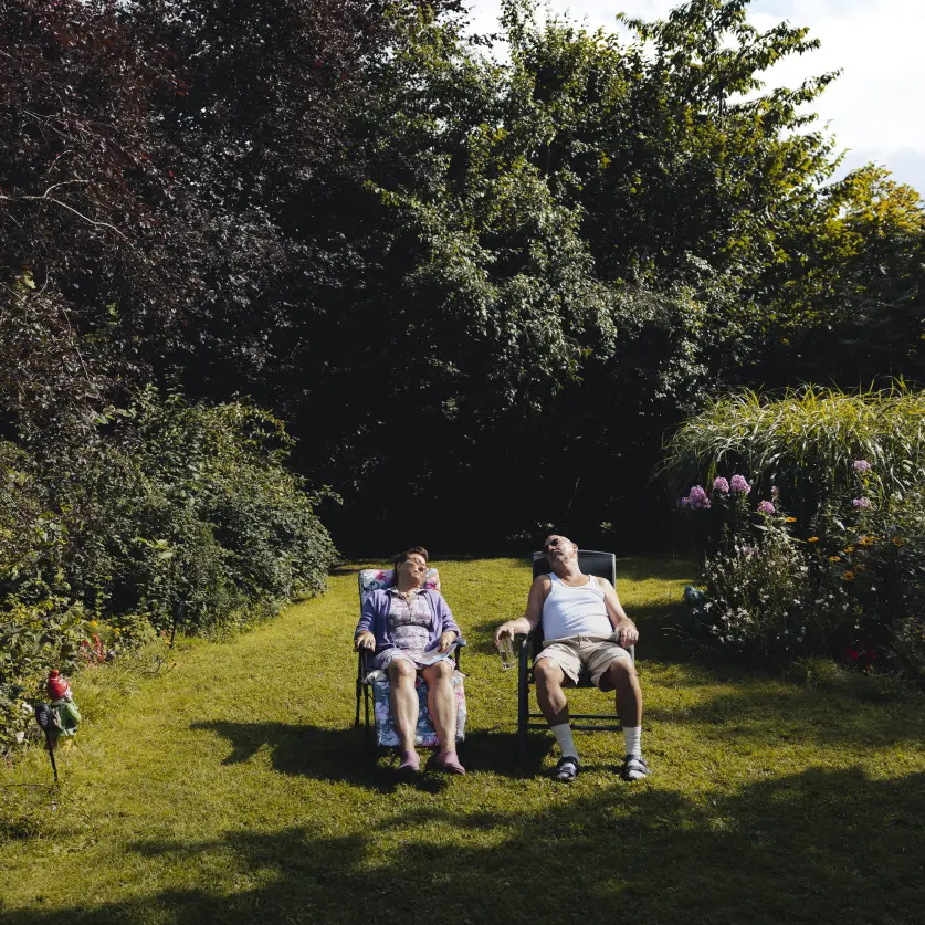 Ein älteres Ehepaar sitzt auf gepolsterten Gartenstühlen in der Sonne auf dem Rasen und macht ein Nickerchen.