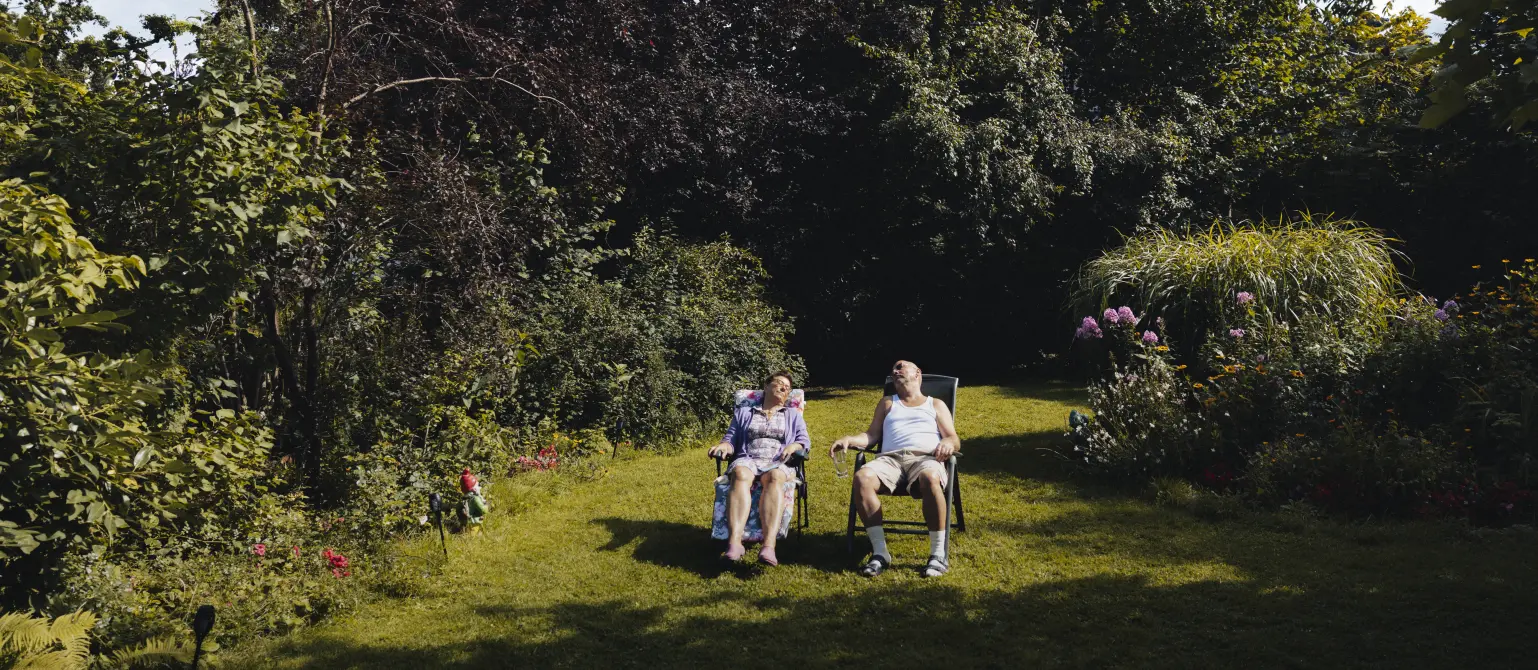 Ein Pärchen liegt in einem großen grünen Garten auf ihren Gartenstühlen und genießt die Sonne