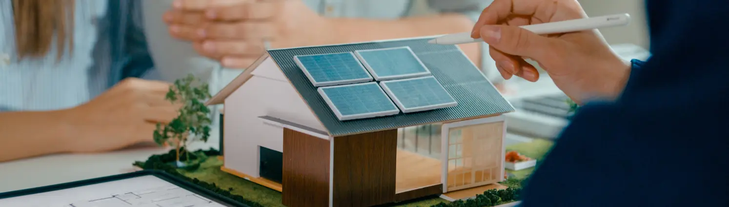 Drei Planerinnen und Planer sitzen um das Modell eines Einfamilienhauses mit Solaranlage auf dem Dach und beraten.