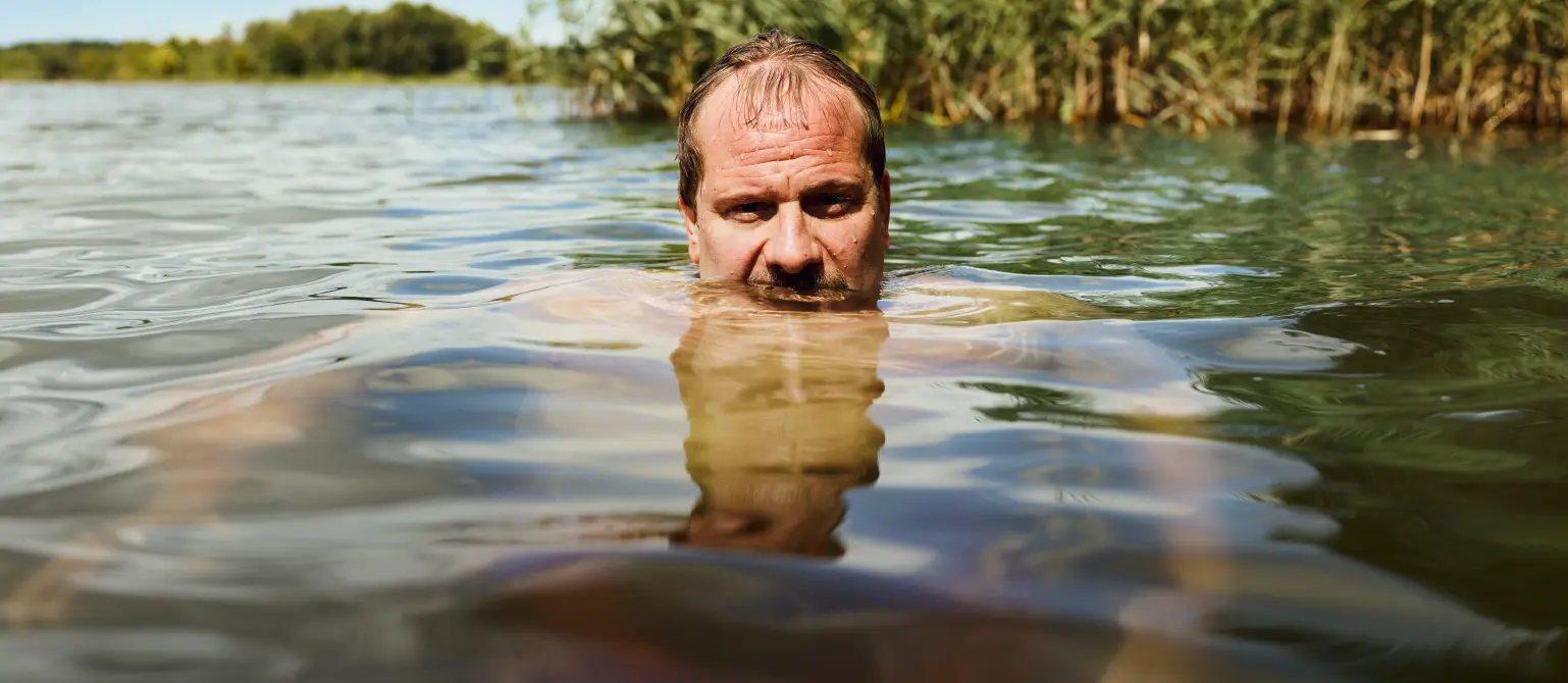 Ein beleibter Mann mit Halbglatze schwimmt in einem Brandenburger See. Arme und Körper sind unter der Wasseroberfläche zu sehen.