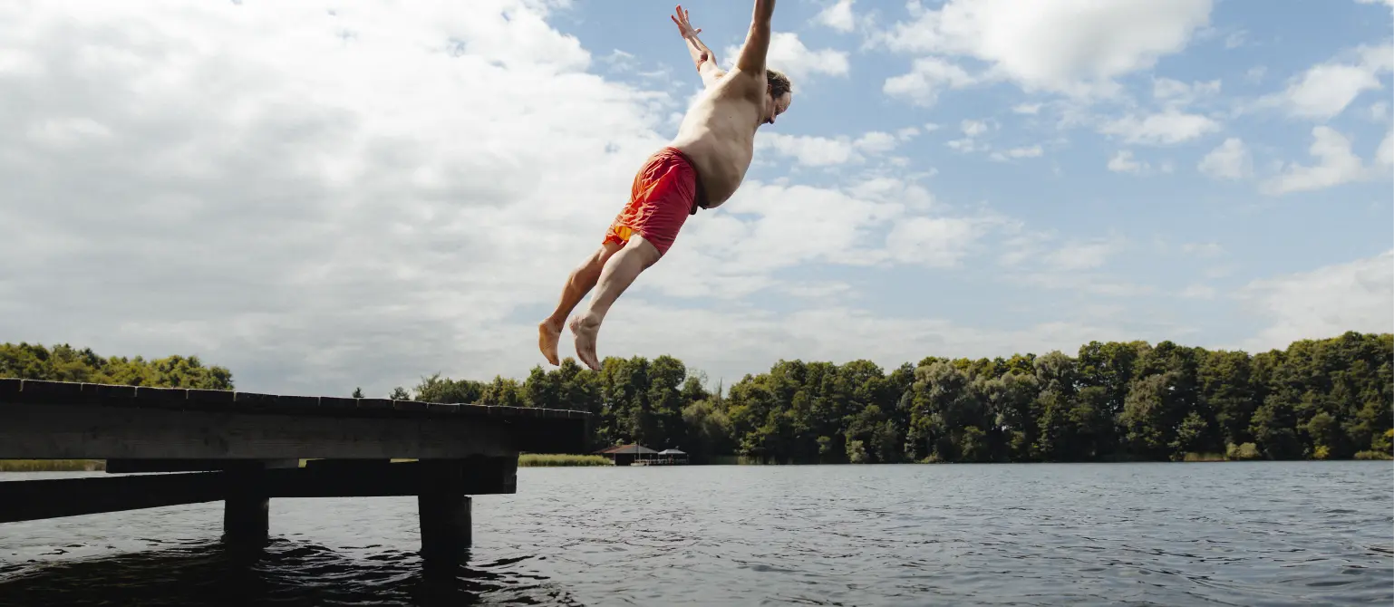 Beleibter Mann in Badehose springt an einem Brandenburger See vom Steg.