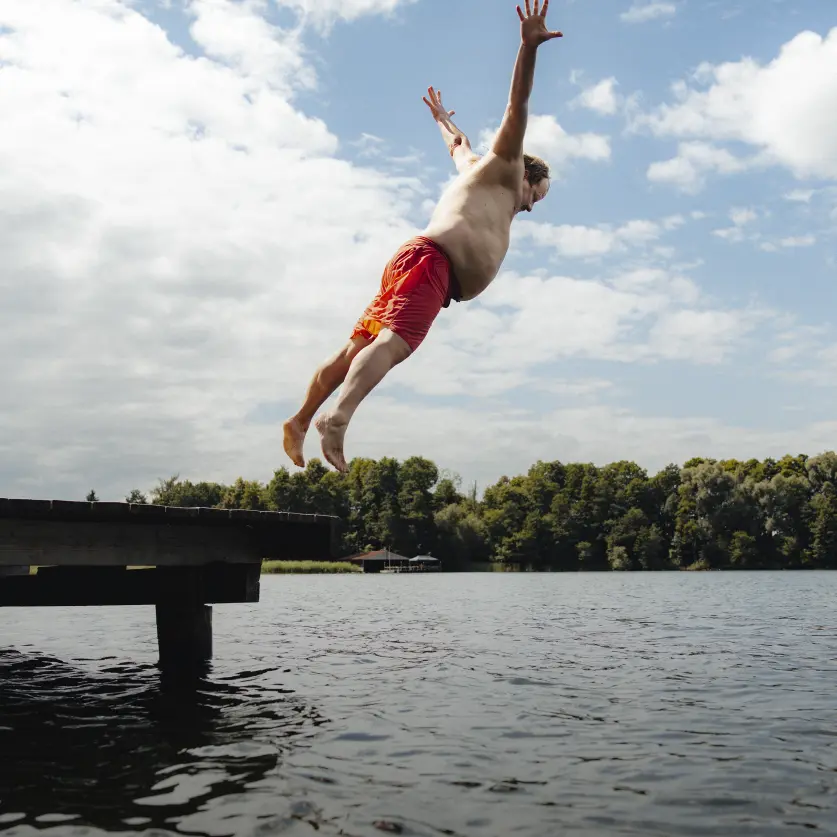 Beleibter Mann in Badehose springt an einem Brandenburger See vom Steg.
