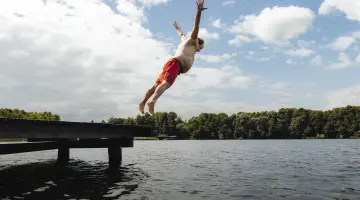 Beleibter Mann in Badehose springt an einem Brandenburger See vom Steg.