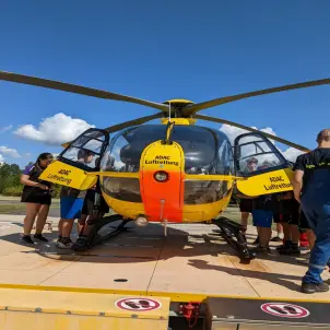 Kinder besichtigen beim Sommercamp der Jugendfeuerwehr Crinitz einen gelben Rettungshubschrauber.