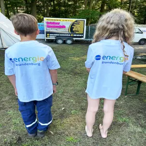 Ein Junge und ein Mädchen stehen mit dem Rücken zur Kamera und zeigen ihr neues T-Shirt mit dem aufgedruckten Energie Brandenburg-Logo.