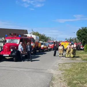 Feuerwehrwagen am Rand einer Straße umgeben von Feuerwehrleuten