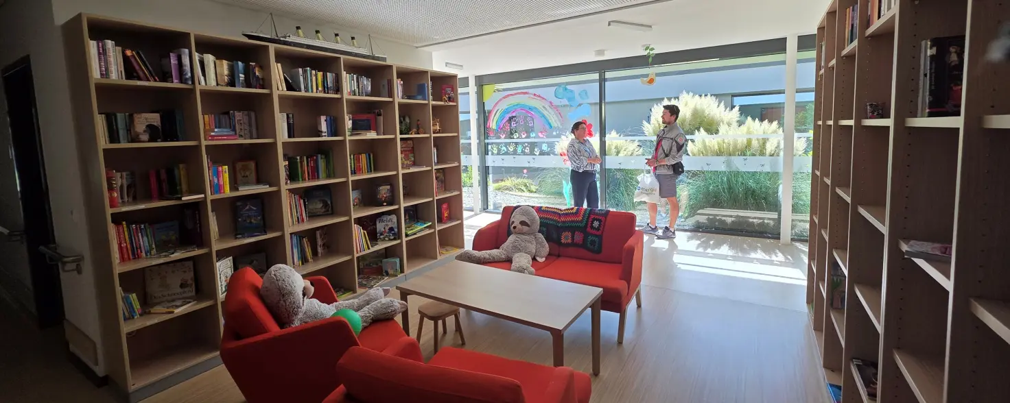 Leseecke mit Sesseln im Kinderhaus Pusteblume: An einer Fensterfront stehen zwei Menschen, die sich miteinander unterhalten.