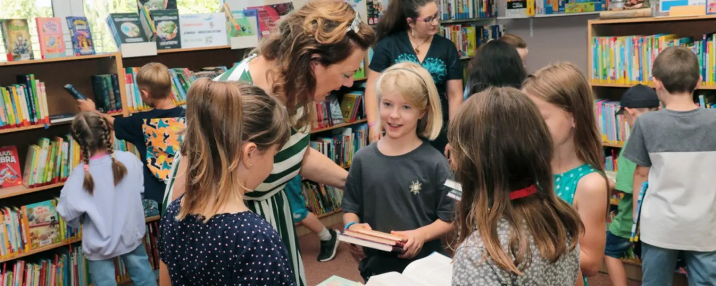 Eine Bibliothekarin berät beim Brandenburger Lesesommer eine Gruppe von Kindern bei der Auswahl ihrer Bücher.