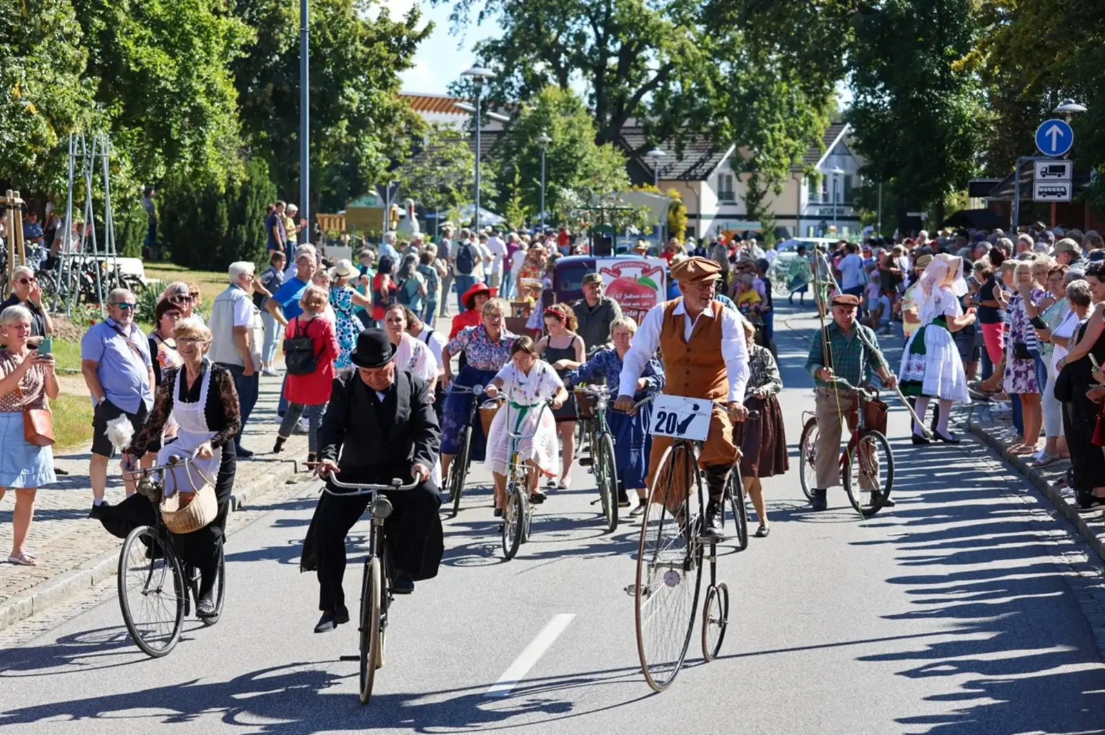 Mit unterschiedlichen Fahrrädern aus vergangenen Zeiten radeln Menschen in historischer Kleidung durch Burg.