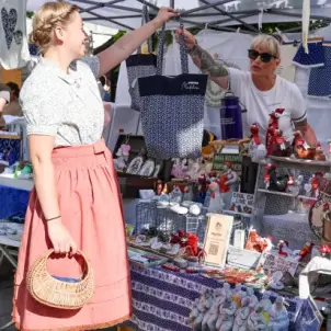 Eine Frau in Tracht kauft an einem Marktstand eine selbstgenähte Tasche.