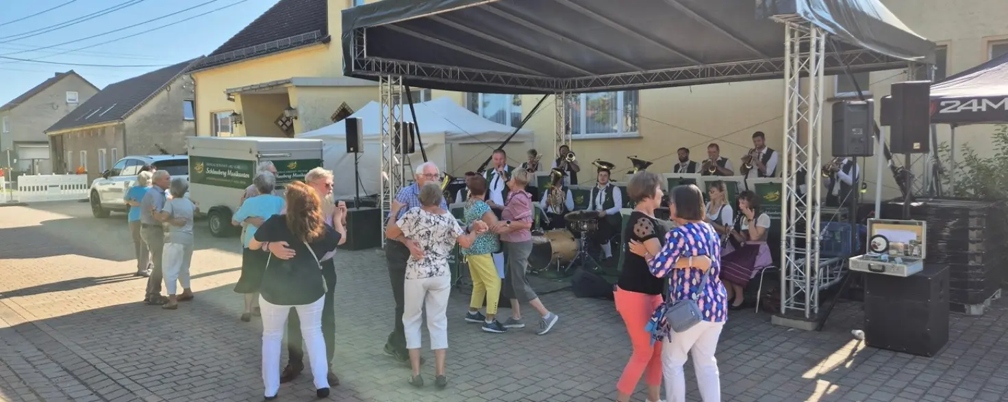 Musiker spielen Musik auf einer Bühne und Menschen tanzen zu zweit auf einem Platz vor der Bühne