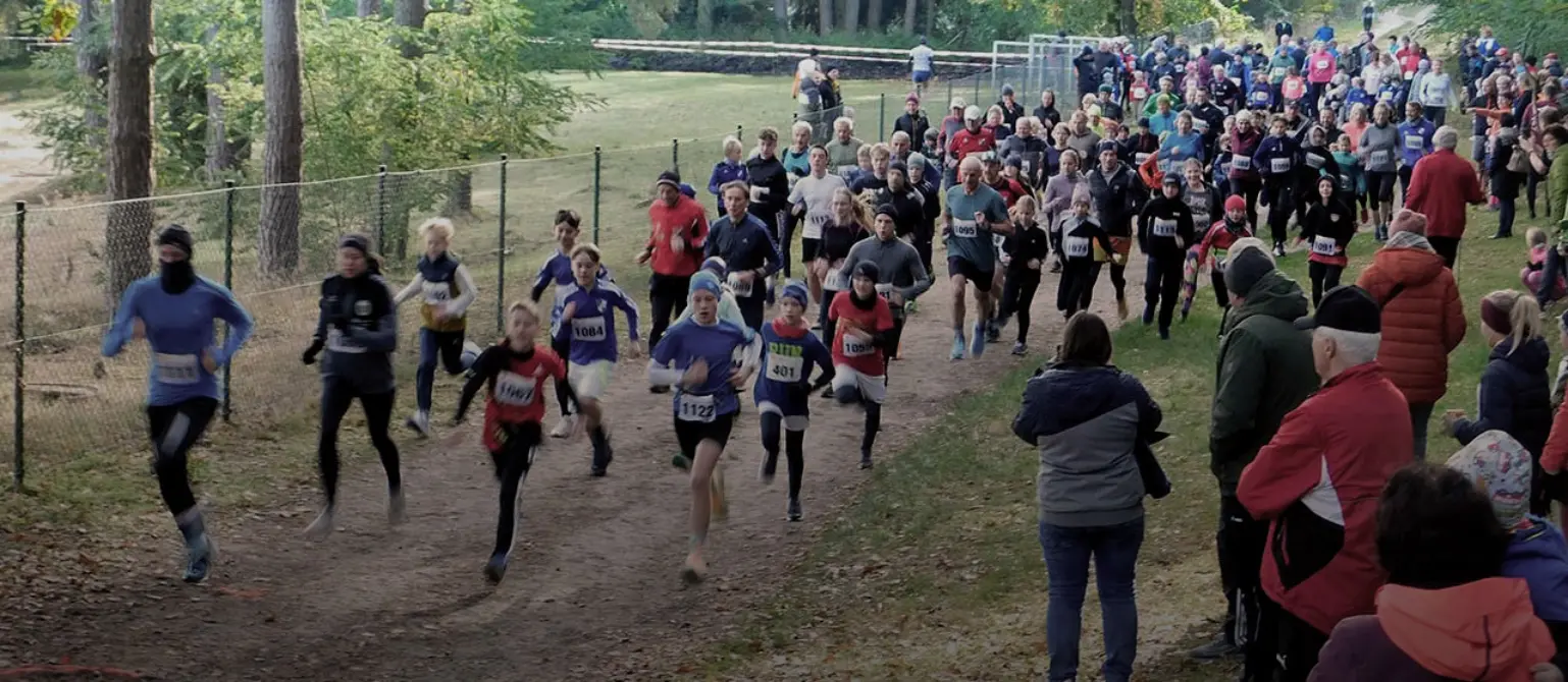 Eine Gruppe von Laufenden in Sportkleidung joggt einen Feldweg entlang. Zuschauer stehen am Rand.