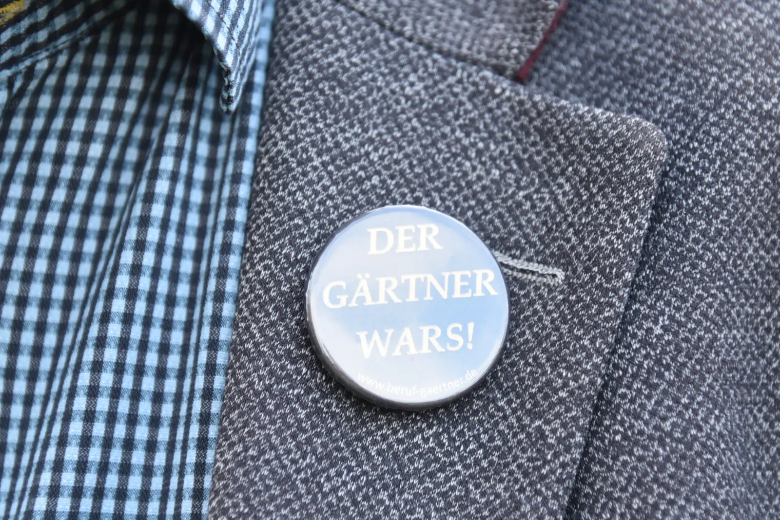 Nahaufnahme von der Jacke eines Mannes, an der ein blauer Ansteckbutton mit der Aufschrift 