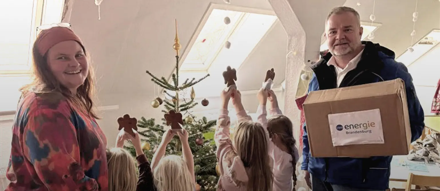 Leiterin Susanne Zechlin und Nick Wichmann lachen in die Kamera während die Kinder fröhlich ihre Lebkuchen dem Weihnachtsbaum präsentieren