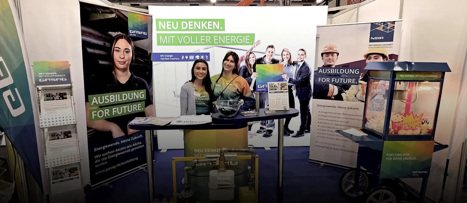 Messestand der Energie Brandenburg bei der Impuls-Messe in Cottbus: Zwei Ausbildungsberaterinnen stehen Arm in Arm am Stand und lächeln.