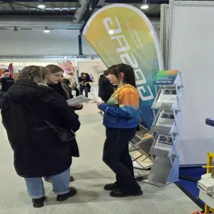 Messestand der Energie Brandenburg mit einer Beraterin im farbigen Hoodie, die mit zwei Interessierten spricht.