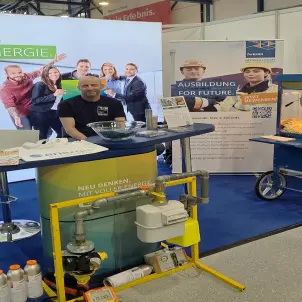 Messestand von Energie Brandenburg mit Infotresen, Technikmodellen und Roll-ups zur Ausbildung. Ein Mann steht hinter dem Tresen mit Infomaterial.