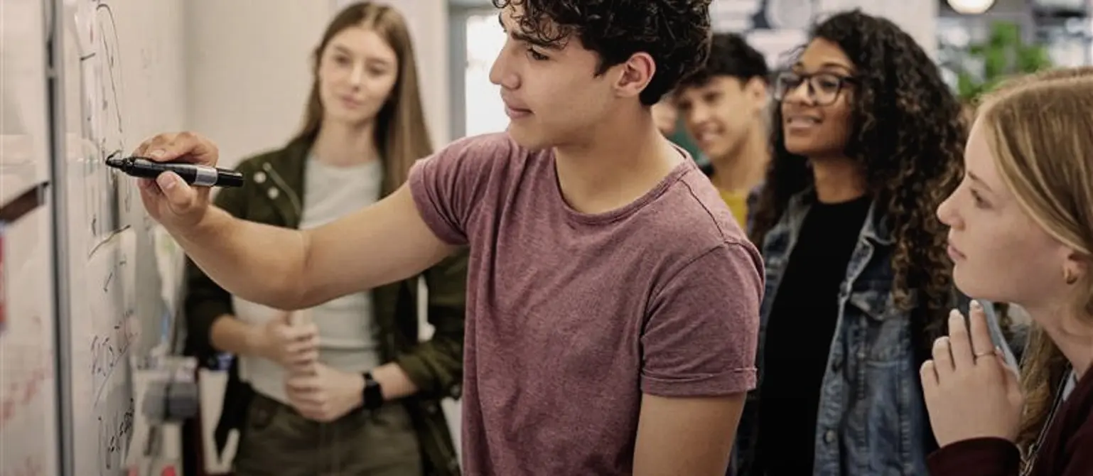 Schülerinnen und Schüler im Teenageralter notieren mit einem Marker wichtige Stichpunkte auf einem Whiteboard.