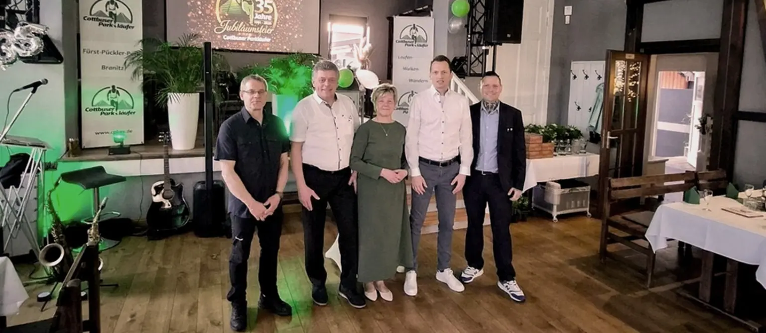 35 Jahre Cottbuser Parkläufer: Vier Personen stehen in einer Reihe vor einer kleinen Bühne in einem Festsaal.