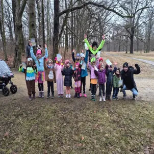 Dreizehn verkleidete Kinder stehen auf einem Waldweg und halten die Hände in die Luft.