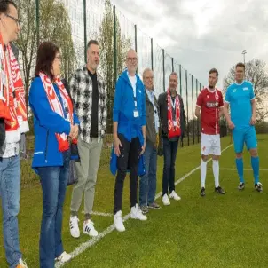 Acht Personen stehen am Rand eines Fußballplatzes in Sportsachen und Fan-Merchandise des FC Energie Cottbus.