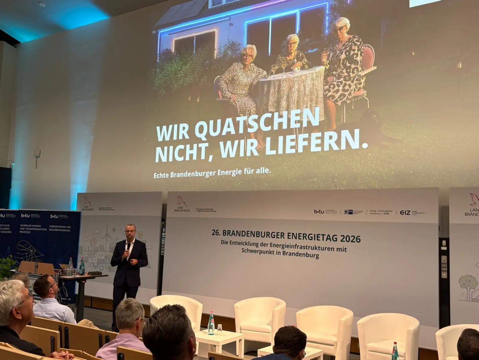 Ein Mann hält auf einer Bühne vor einem Publikum einen Vortrag.