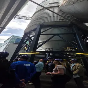 Besuchergruppe mit Schutzhelmen besichtigt die thermische Abfallbehandlungsanlage Lauta mit zylindrischem Silo und Rohrleitungen.