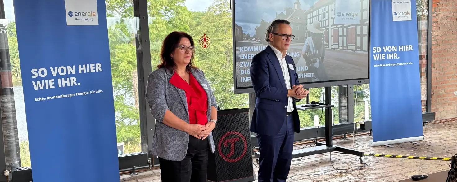 Eine Frau und ein Mann stehen vor einem Bildschirm und sprechen zum Publikum.