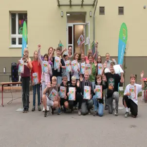 Eine Schulklasse steht vor der Schule und hält Urkunden für den erste Platz hoch.