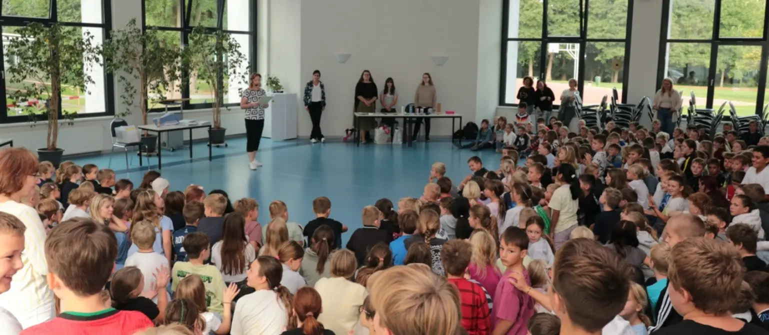 Kinder sitzen in einer großen Halle gemeinsam in einem Halbkreis.
