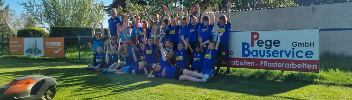 Ein Mähroboter fährt über die große Fußballfläche und die TSV Mannschaft hat sich jubelnd hinter ihm aufgereiht zum Gruppenfoto