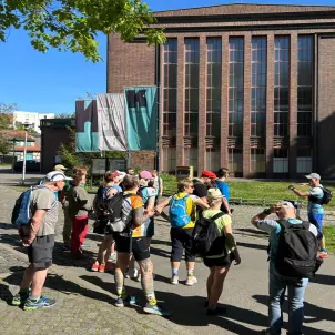 Die Wandergruppe steht vor dem Baudenkmal Dieselkraftwerk