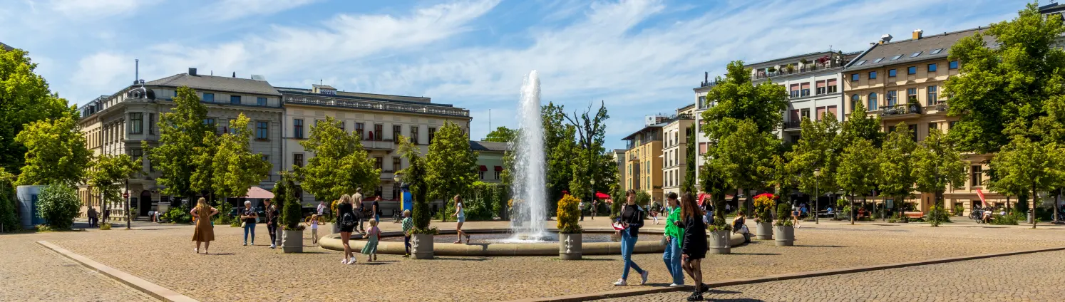 Sommertag, an dem vergnügte Menschen am Brunnen auf dem Louisenplatz in Brandenburgs Hauptstadt Potsdam flanieren.