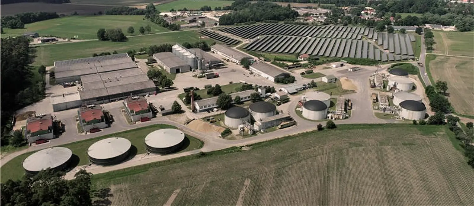 Luftansicht der Biogasanlage der DAH Gruppe im brandenburgischen Putlitz bei blauem Himmel. Drumherum grüne Felder.